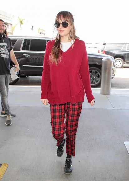 Dakota Johnson walking at an airport while wearing red and black plaid pants and a red sweater 