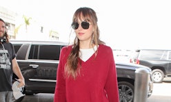 Dakota Johnson wearing dark shades, a white t-shirt beneath a red long-sleeved sweater at the airpor...