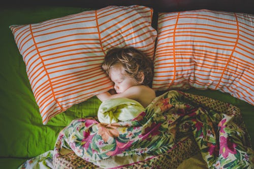 A little kid sleeping on two large striped pillows, under a floral blanket