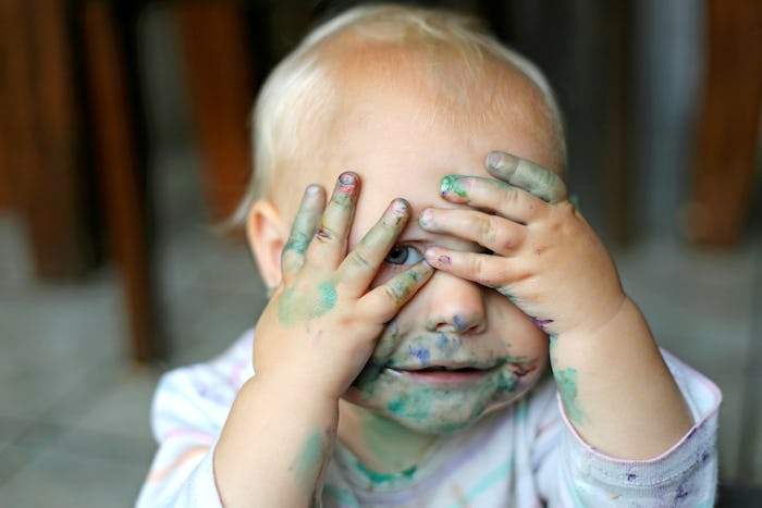 Baby covering face with hands while having paint all over himself