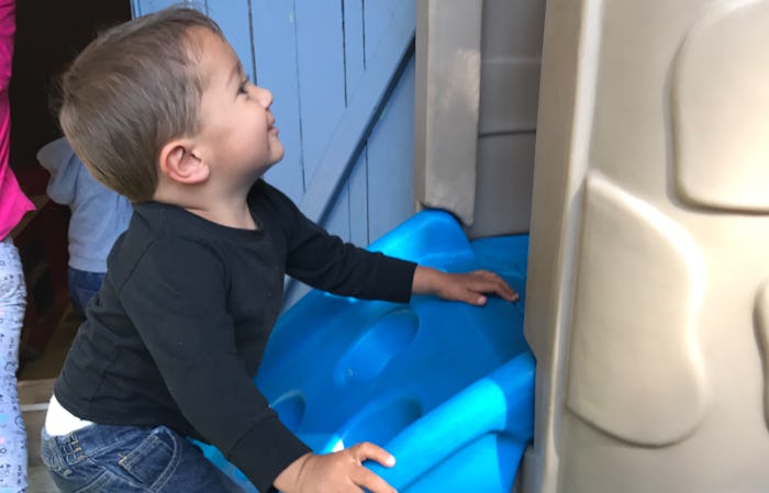 A toddler boy climbing a blue mini slide