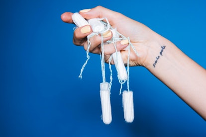 A womans hand holding a lot of tampons in front of a dark blue background