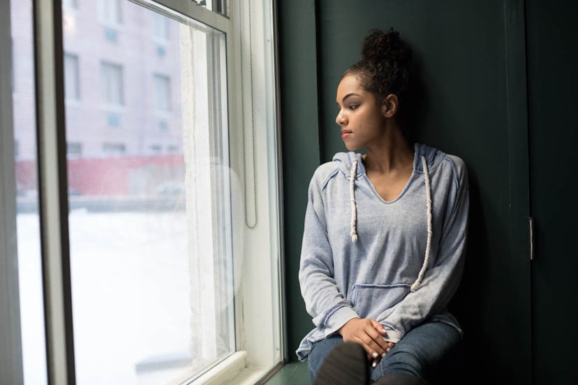 A woman in a grey sweatshirt sitting at a windowsill looking out of the window