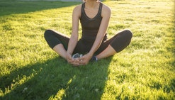 A woman sitting on grass and stretching her hips
