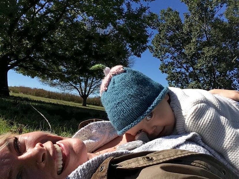 A mom lying on grass with her baby child lying on her chest