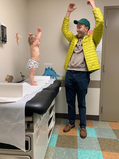 A dad playing with his little daughter while she is standing on a hospital bed