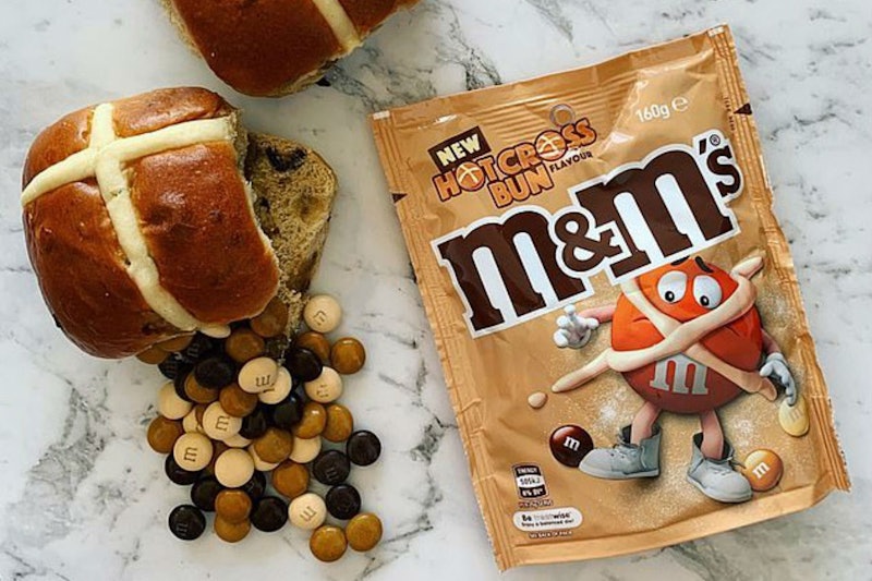 A package of the Hot Cross Bun M&Ms Easter treats next to a real hot cross bun.