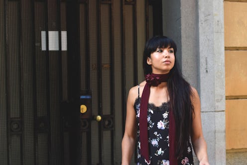 A young black-haired female barista wearing a floral-patterned slip dress with a burgundy scarf