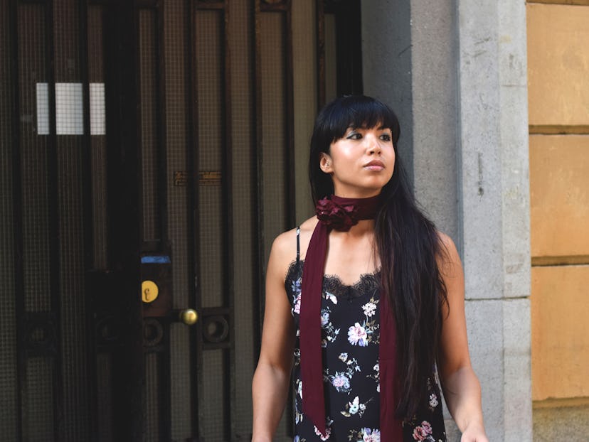 A young black-haired female barista wearing a floral-patterned slip dress with a burgundy scarf