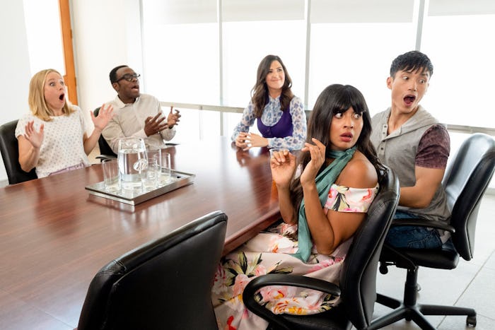 A scene from the show 'The Good Place' with the cast members sitting at a desk and looking surprised