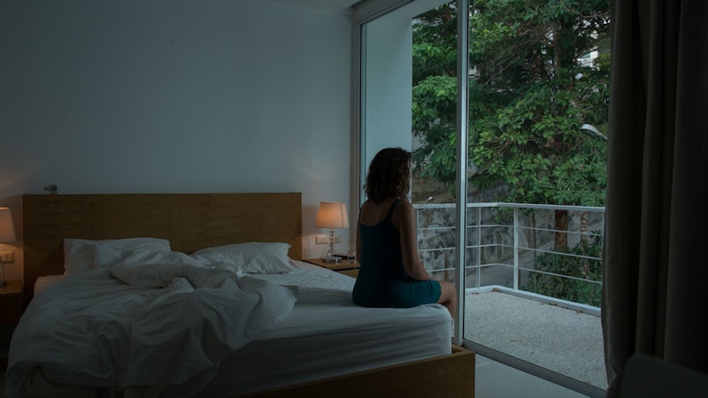 A woman with SAD sitting on the edge of her bed looking out of the window