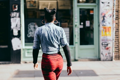 A woman with SAD in a blue dress shirt and red pants walking down the street