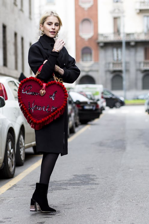 A woman who is single for valentine's day in a black coat and boots and a red heart-shaped bag