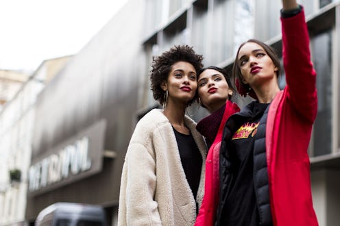 Three women taking a selfie while pouting their lips and standing next to each other on the street