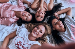 Four single friends; women lying on a bed with their heads close to each other on Valentine's Day