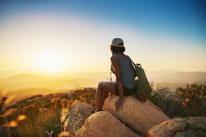 A woman sitting on a rock looking at the sunset after a hike