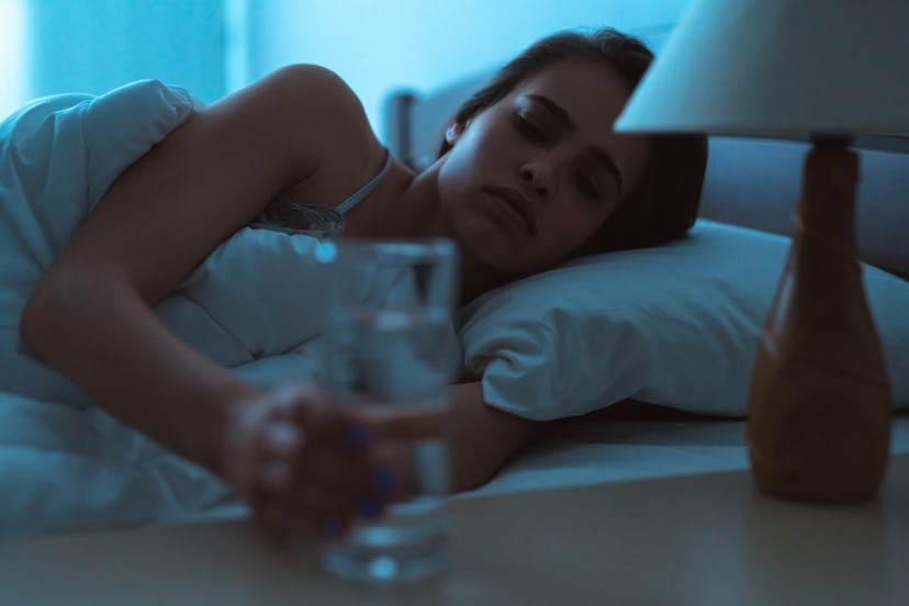 A woman taking a glass of water from her bed