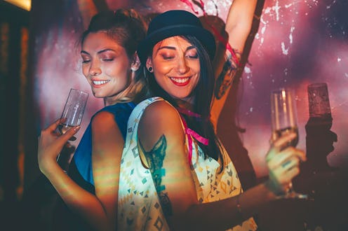 Two girls dancing on a party while holding glasses of Champaign.