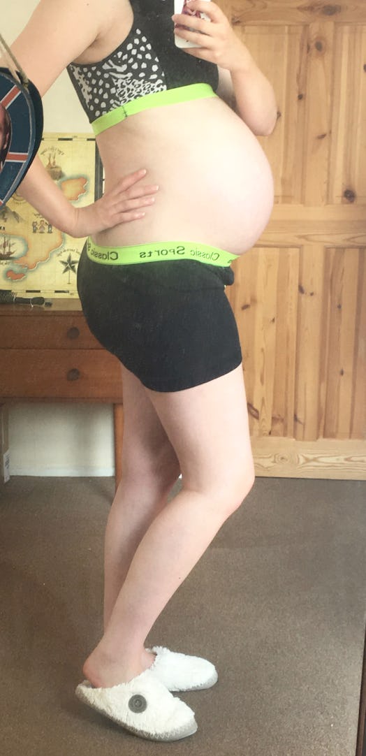 A pregnant woman taking a mirror selfie while wearing a black sport top and pants combination