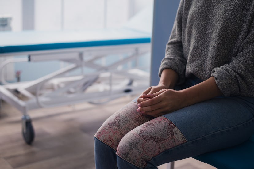 A woman sitting in a hallway at a hospital with her hands on her lap