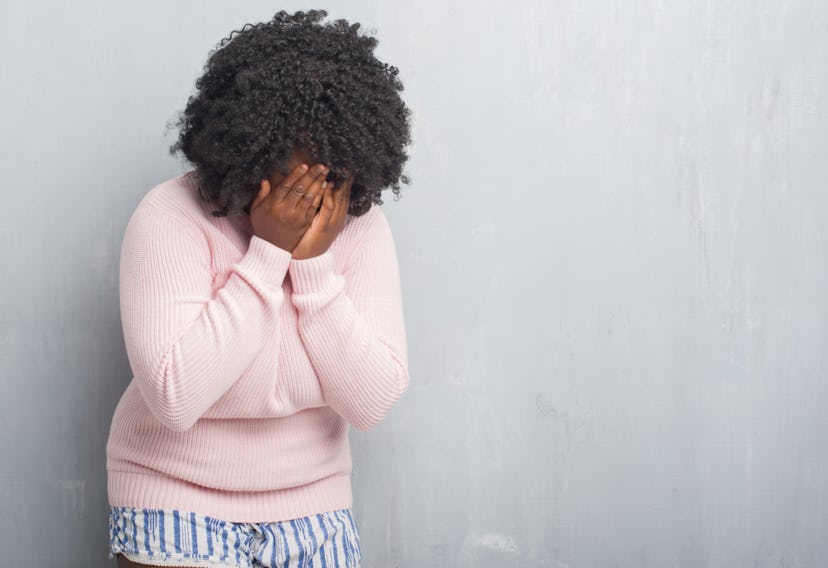 A curly-haired woman in a pink sweater with her hands on her face while crying due to Lyme disease