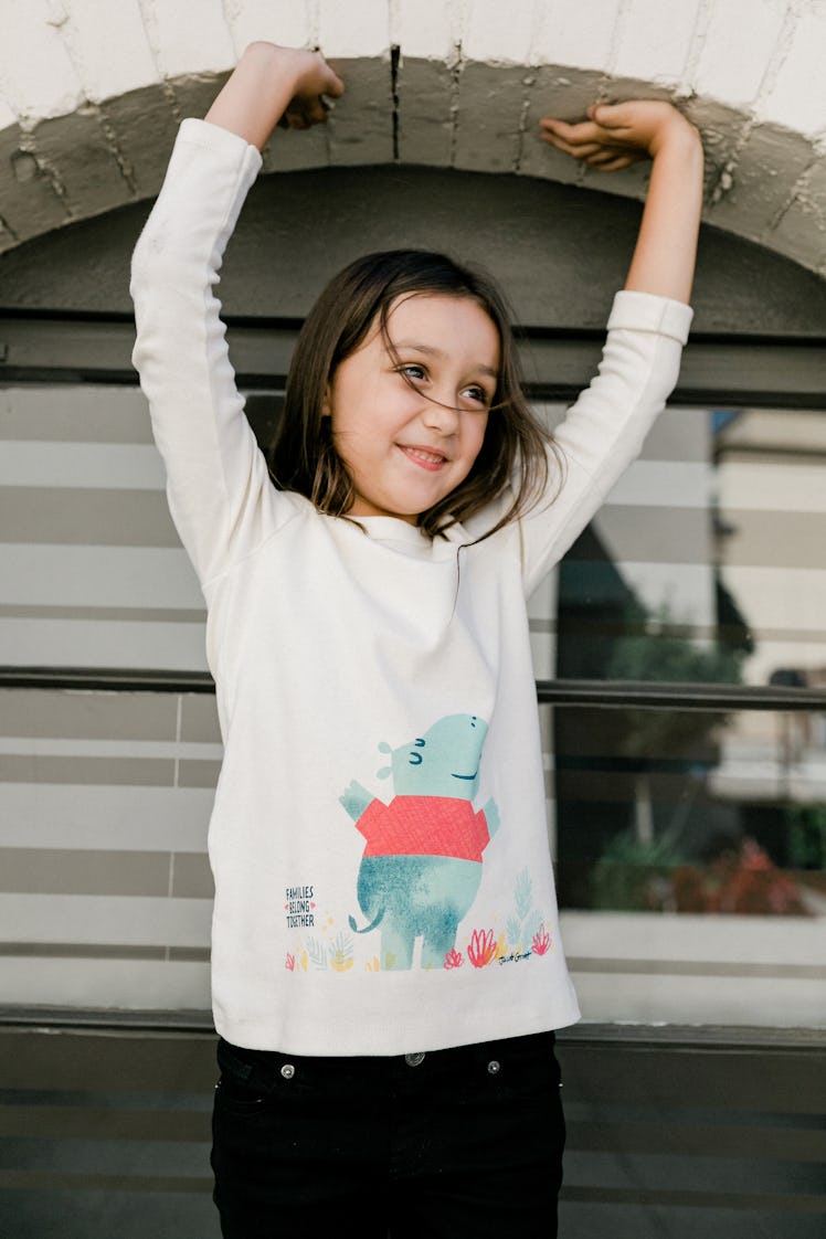 A little girl posing in a Winter Water Factory x Families Belong Together capsule collection white s...
