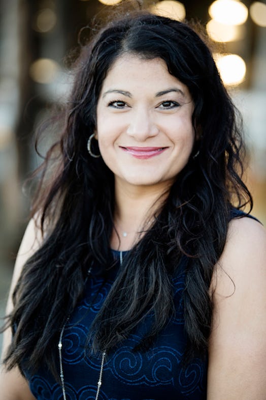 A closeup of Amisha Klawonn smiling with her hair down and in a black blouse with silver hoop earrin...