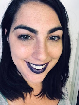 A picture of a woman in her 30s, brown hair, purple lipstick, proudly rocking her witch vibe.