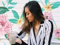Woman holding a drink posing in front of a floral wall outside, which is one of the coolest secret I...