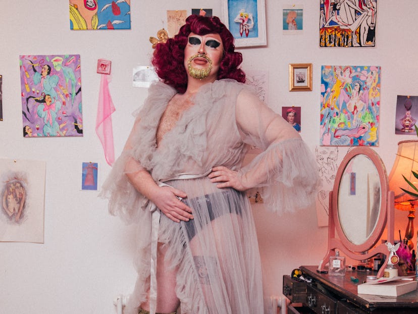 Tom Rasmussen, with strong makeup and a red wig, wearing a sheer pale pink robe with frills in his b...