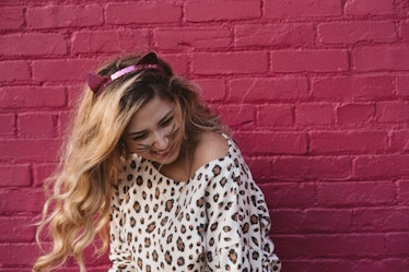 A girl with blonde hair posing in a cat costume and laughing in front of a pink wall is a great pose...