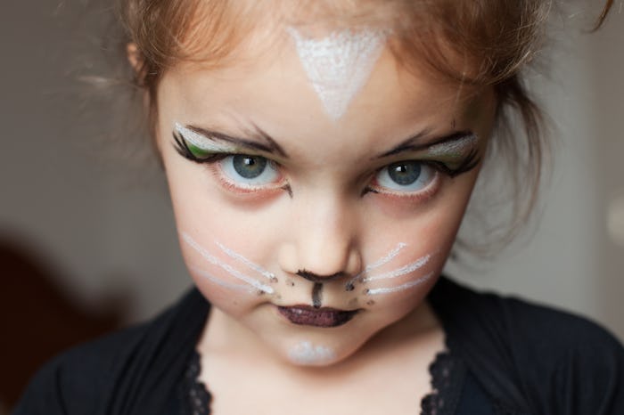 A little girl dressed as a cat with cat makeup looking at camera.