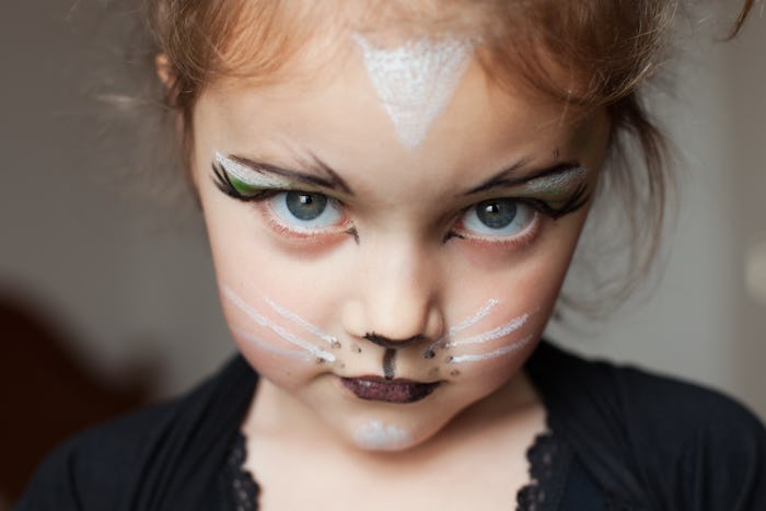 A little girl dressed as a cat with cat makeup looking at camera. 