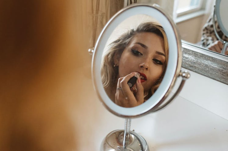 A blonde girl applies red lipstick in the mirror while she gets ready.