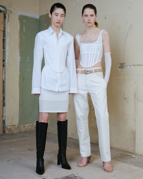 Two models posing next to each other in an empty room, both wearing white outfits