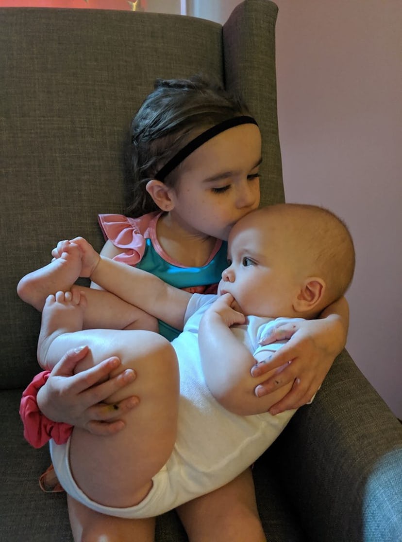An older sister holding her baby sibling and kissing him on the head.