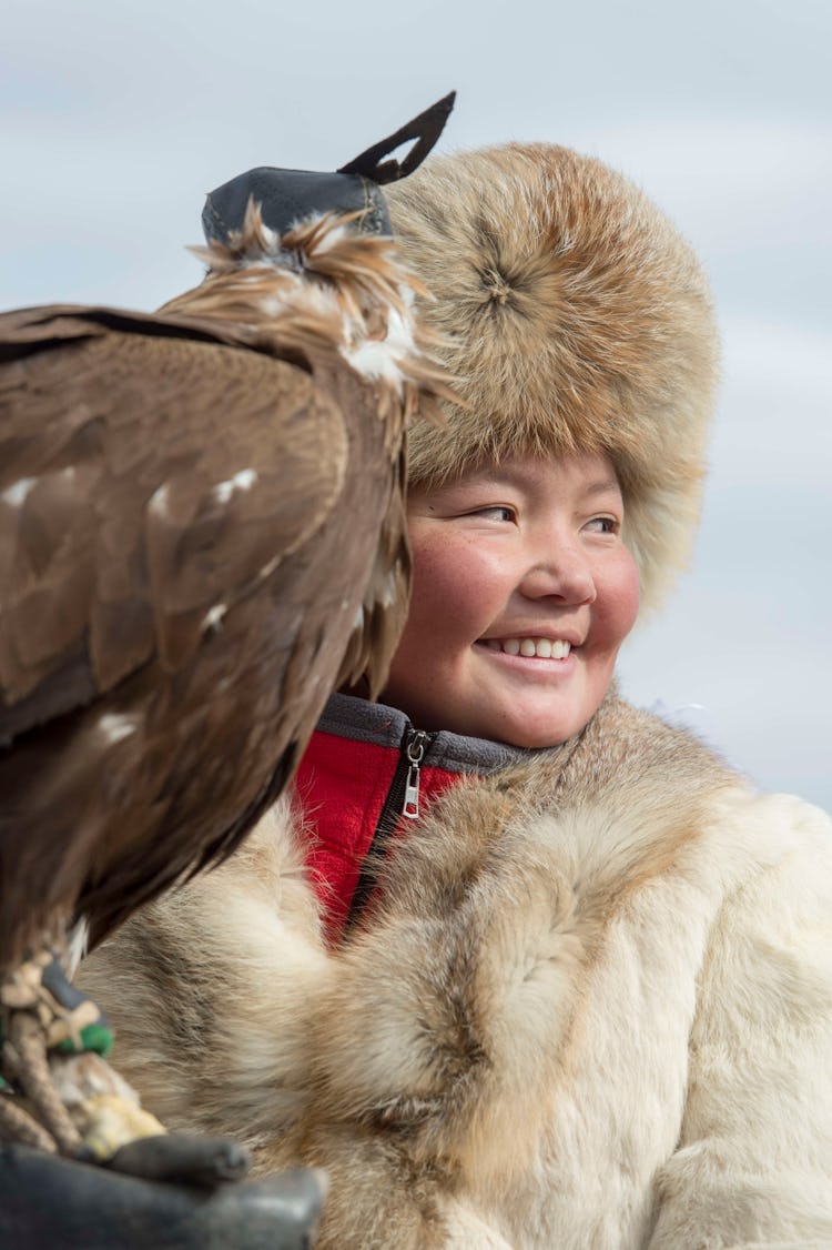 Mongolian girl proudly holds eagle on her arm.