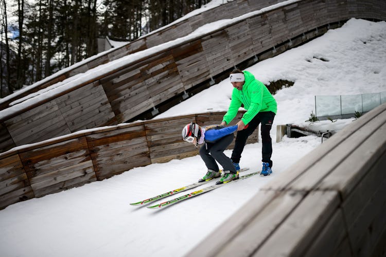 A young female ski jumper crouches as she prepares to shoot off a nordic jump with her coach.