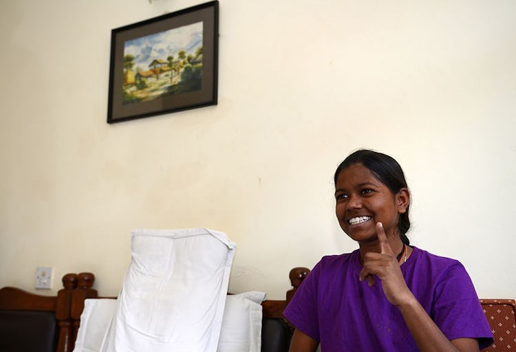 Indian girl mountaineer sits on couch smiling with finger raised.