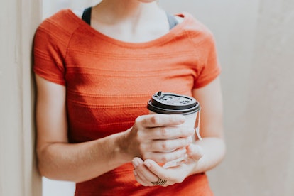 A girl is holding a latte in a to-go cup and wearing an orange shirt.