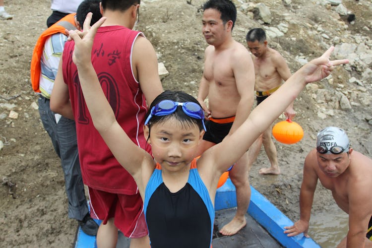 girl in swimmers raises her hands in triumph after crossing river.