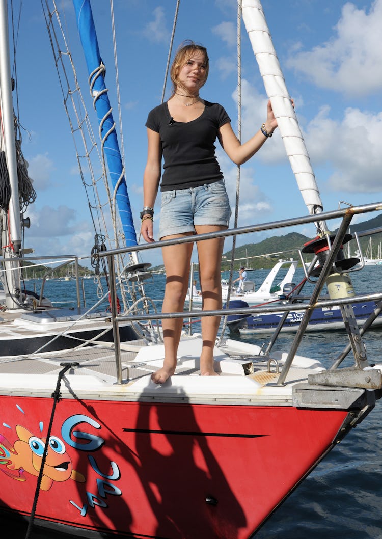 Girl stands on bow of yacht as it enters a harbor.