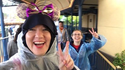 Two friends waiting in line at Disney wearing rain ponchos and holding up peace signs.