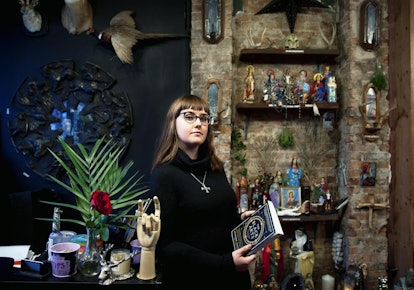A brunette woman dressed in a black sweater and glasses holds a book on black arts in a studio.