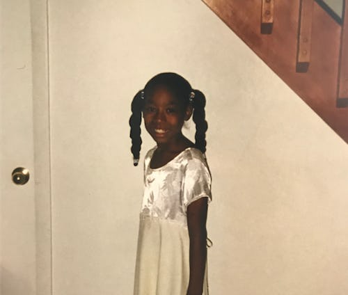 The author as a young child, standing in a white dress smiling at the camera. 