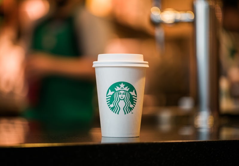 A white, paper Starbucks hot cup with the green siren logo on it sitting on a tabletop.