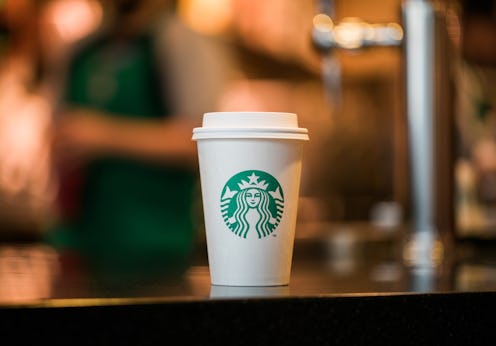 A white, paper Starbucks hot cup with the green siren logo on it sitting on a tabletop.