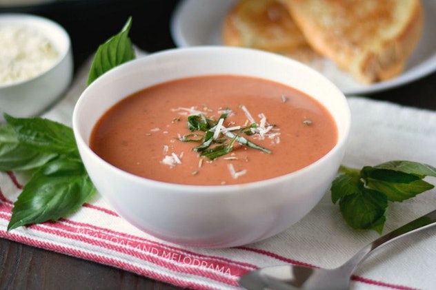 Tomato soup in a white bowl with grilled cheese sandwich in the background.