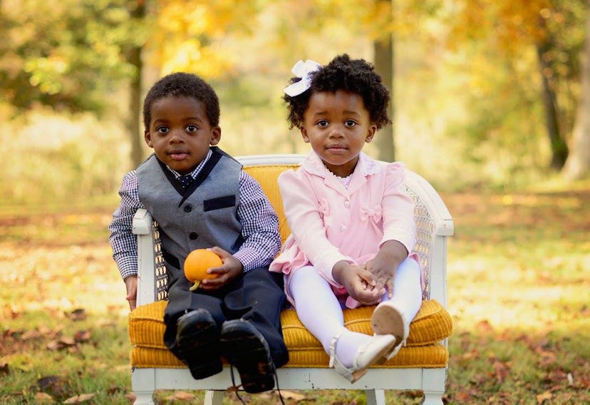 Little girl and little boy sit on tiny sofa on grass.