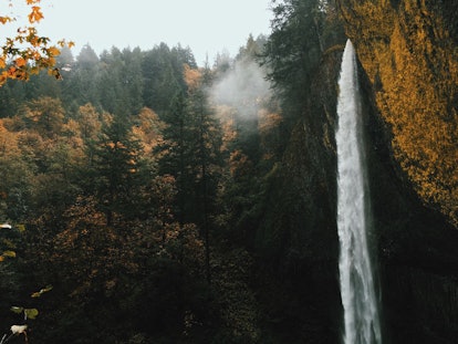 A waterfall in the Columbia River Gorge in Oregon is surrounded by fall foliage, mist, and sunshine.